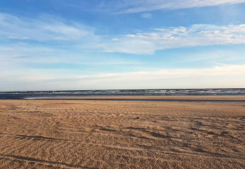 Plage paisible avec sable doré et mer calme sous un ciel bleu, photo prise depuis un lodge.