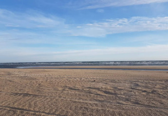 Ruhiger Sandstrand mit sanften Wellen und blauem Himmel, fotografiert nahe einer Lodge am Meer.