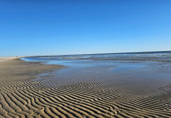 Wunderschöner Blick auf den Strand bei Ebbe an einer Lodge, mit Sandrillen und klarem blauen Himmel.