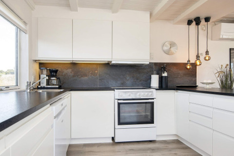 Moderne Küche in Seaside Charm in Rindby, Dänemark, mit weißen Schränken und eleganten Hängeleuchten.