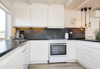 Moderne Küche in Seaside Charm in Rindby, Dänemark, mit weißen Schränken und eleganten Hängeleuchten.