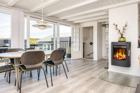 Helles Esszimmer mit Kamin und großen Fenstern in der Lodge Seaside Charm in Rindby, Dänemark.