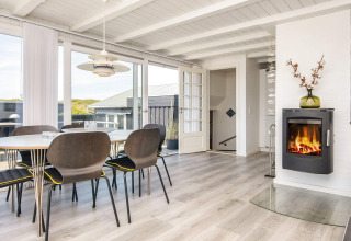 Helles Esszimmer mit Kamin und großen Fenstern in der Lodge Seaside Charm in Rindby, Dänemark.
