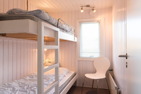 Helles Zimmer mit Etagenbett, weißem Stuhl und Fenster in Seaside Charm in Rindby, Dänemark.