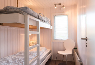 Helles Zimmer mit Etagenbett, weißem Stuhl und Fenster in Seaside Charm in Rindby, Dänemark.