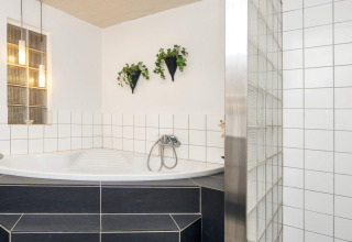 Helles Badezimmer in Seaside Charm in Rindby, Dänemark, mit Eckbadewanne, weißen Fliesen und Hängepflanzen.