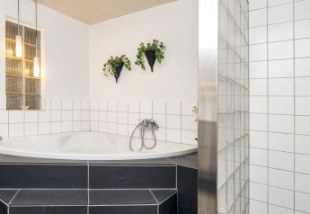Helles Badezimmer in Seaside Charm in Rindby, Dänemark, mit Eckbadewanne, weißen Fliesen und Hängepflanzen.