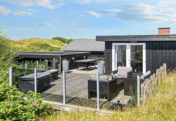 Terrasse eines dunkel gestrichenen Ferienhauses in Rindby, Dänemark, umgeben von Dünen und Natur.