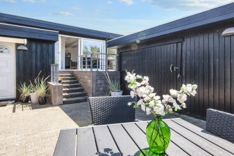 Sonnige Terrasse bei Seaside Charm in Rindby, Dänemark, mit schwarzer Fassade und grüner Blumenvase.