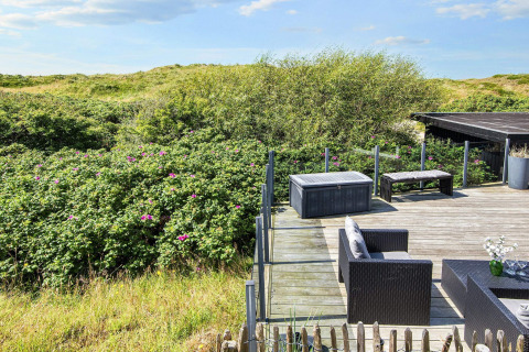 Sonnige Terrasse mit Gartenmöbeln und Blick auf grüne Dünen bei Seaside Charm in Rindby, Dänemark.