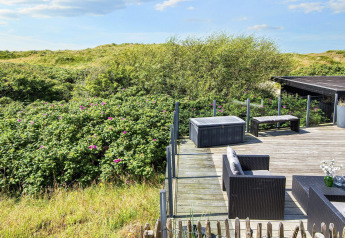 Sonnige Terrasse mit Gartenmöbeln und Blick auf grüne Dünen bei Seaside Charm in Rindby, Dänemark.
