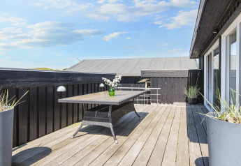 Holzterrasse mit schwarzem Zaun und modernem Gartentisch an der Seaside Charm Lodge in Rindby, Dänemark.
