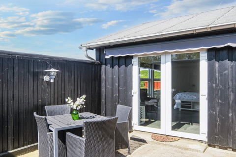 Terrasse im Seaside Charm in Rindby, Dänemark, mit schwarzen Möbeln, Blumen und Blick ins Zimmer.