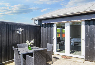 Terrasse im Seaside Charm in Rindby, Dänemark, mit schwarzen Möbeln, Blumen und Blick ins Zimmer.