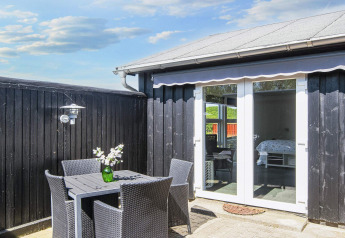 Terrasse im Seaside Charm in Rindby, Dänemark, mit schwarzen Möbeln, Blumen und Blick ins Zimmer.