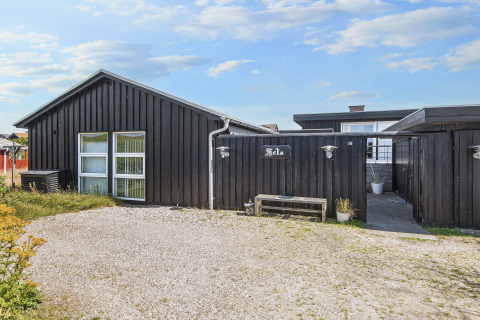 Außenansicht der Lodge Seaside Charm in Rindby, Dänemark, mit schwarzer Fassade und Kiesweg.