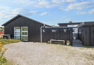 Außenansicht der Lodge Seaside Charm in Rindby, Dänemark, mit schwarzer Fassade und Kiesweg.