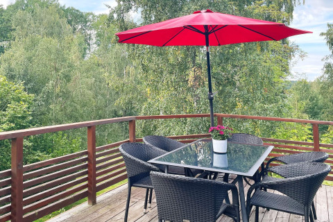 Terrazza della casa vacanze a Gränna, Svezia, con tavolo in vetro, sedie nere, ombrellone rosso e vista sui boschi.