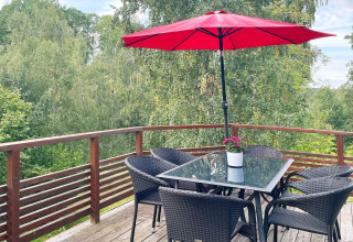 Buitenterras bij vakantiehuis in Gränna, Zweden, met glazen tafel, stoelen, rode parasol en uitzicht op bos.