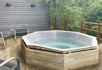 Bain à remous extérieur sur une terrasse en bois d'une maison de vacances à Gränna, Suède, entouré de verdure.