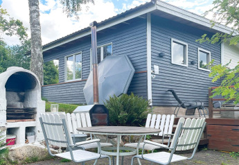 Udendørs gårdhave med spisebord, stole og grill foran et sommerhus i Gränna, Sverige.