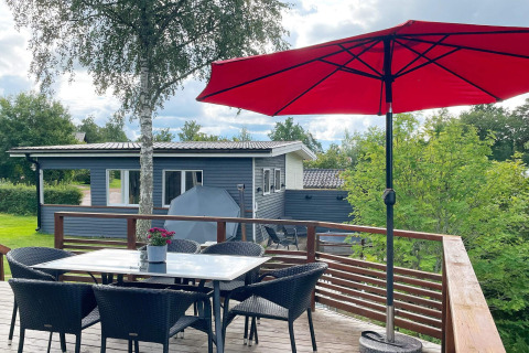 Terrazza esterna casa vacanze a Gränna, Svezia, con ombrellone rosso, tavolo, sedie e tanto verde.