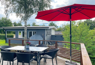Terrazza esterna casa vacanze a Gränna, Svezia, con ombrellone rosso, tavolo, sedie e tanto verde.