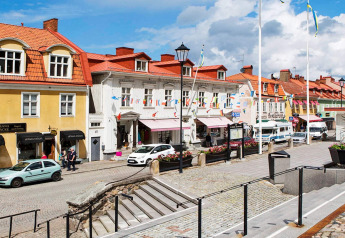Strada pittoresca a Gränna, Svezia, con edifici storici, negozi, auto parcheggiate e cielo nuvoloso luminoso.