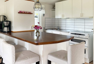 Cucina moderna con penisola, mobili bianchi e vaso di fiori in casa vacanze per 6 persone a Gränna, Svezia.