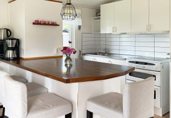 Modern kitchen in 6 person holiday home in Gränna, Sweden, with breakfast bar, white cabinets and a vase of flowers.