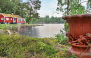 Rotes Ferienhaus am See in Åkersberga, Schweden, mit großer Urne und grüner Natur im Vordergrund.
