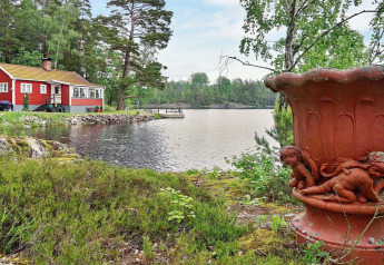 Rotes Ferienhaus am See in Åkersberga, Schweden, mit großer Urne und grüner Natur im Vordergrund.