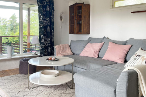 Gemütliches Wohnzimmer in einer Lodge in Gränna, Schweden, mit grauem Sofa, rosa Kissen und großem Fenster.