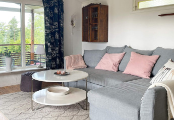 Gemütliches Wohnzimmer in einer Lodge in Gränna, Schweden, mit grauem Sofa, rosa Kissen und großem Fenster.