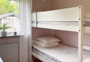 Dormitorio luminoso con litera blanca, papel pintado floral y ventana grande en una casa de vacaciones en Gränna, Suecia.