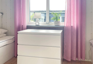 Lichte kamer met witte kast, roze gordijnen, tafellamp en plant in vakantiehuis te Gränna, Zweden.
