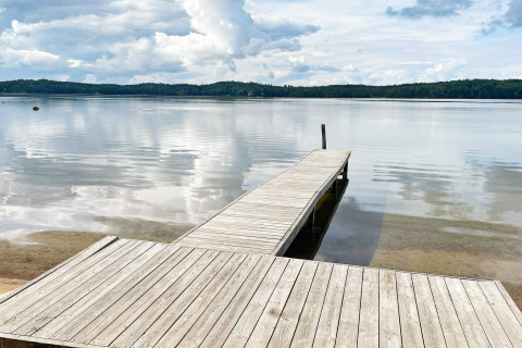 Holzsteg an einem ruhigen See mit bewaldetem Ufer beim 6-Personen-Ferienhaus in Gränna, Schweden.