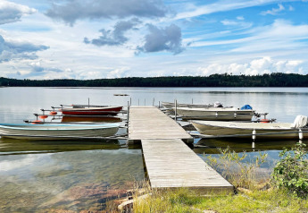 Pont en bois avec barques amarrées sur un lac paisible près du gîte 6 personnes à GRÄNNA, Suède, ciel bleu.