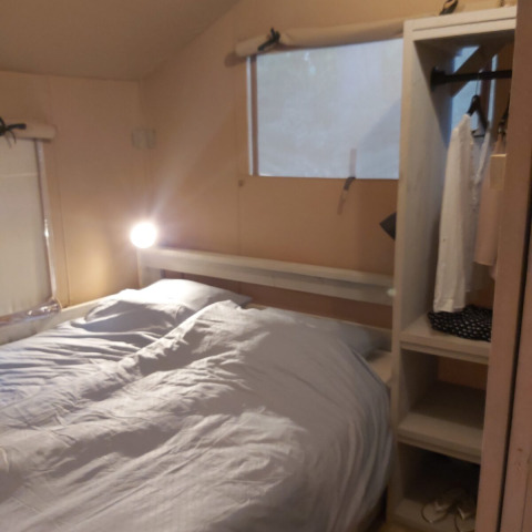 Interior de una tienda safari Ranger Lodge en Petite Suisse, Bélgica, con cama doble, armario y ventana.