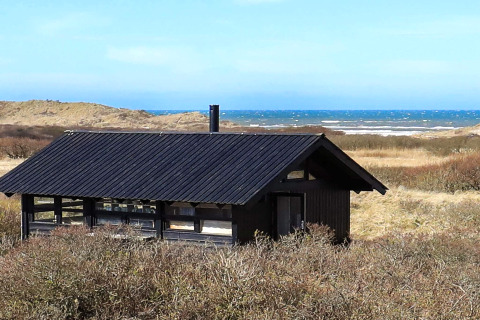 Sommerhus til 4 personer i Bindslev, Danmark, med sort tag, tæt på klitter og havudsigt i baggrunden.
