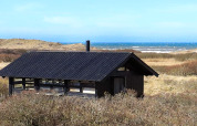Chalet pour 4 personnes à Bindslev, Danemark, toit noir, près des dunes avec vue sur la mer en arrière-plan.