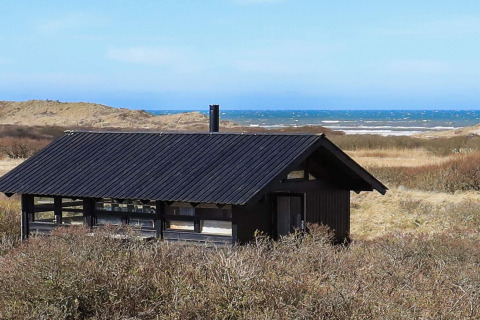 Sommerhus til 4 personer i Bindslev, Danmark, med sort tag, tæt på klitter og havudsigt i baggrunden.