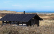 Chalet per 4 persone a Bindslev, Danimarca, tetto nero, circondato da dune e vista mare sullo sfondo.