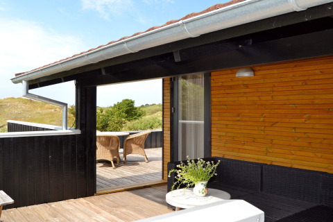 Terrazza in legno con arredi esterni della casa vacanze per 6 persone a Fanø, Danimarca, immersa nel verde.