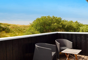 Buitenterras met twee zwarte stoelen en een tafeltje, uitzicht op groene duinen in Fanø, Denemarken.