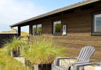 Buitenaanzicht van een 6-persoons vakantiehuis in Fanø, Denemarken, met houten gevel en tuinstoel.