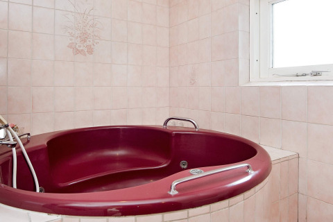 Runde, weinrote Jacuzzi-Badewanne im Badezimmer mit rosa Fliesen und Fenster im Ferienhaus auf Fanø, Dänemark.