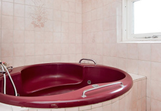 Runde, weinrote Jacuzzi-Badewanne im Badezimmer mit rosa Fliesen und Fenster im Ferienhaus auf Fanø, Dänemark.