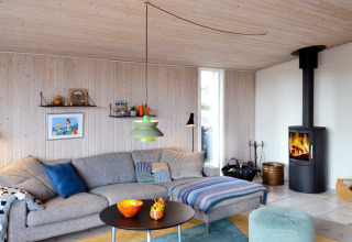 Wohnzimmer in einem Ferienhaus auf Fanø, Dänemark mit grauem Sofa, Holzofen und moderner Deko.