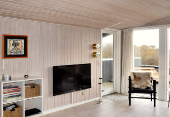 Stue i feriebolig i Fanø med vægmonteret tv, sort stol med pels, udsigt til terrasse og moderne indretning.